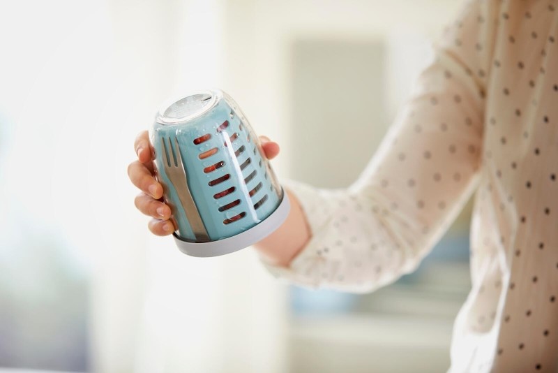 Blauer Mepal To-Go-Becher in der Hand einer Person mit gepunktetem Oberteil.