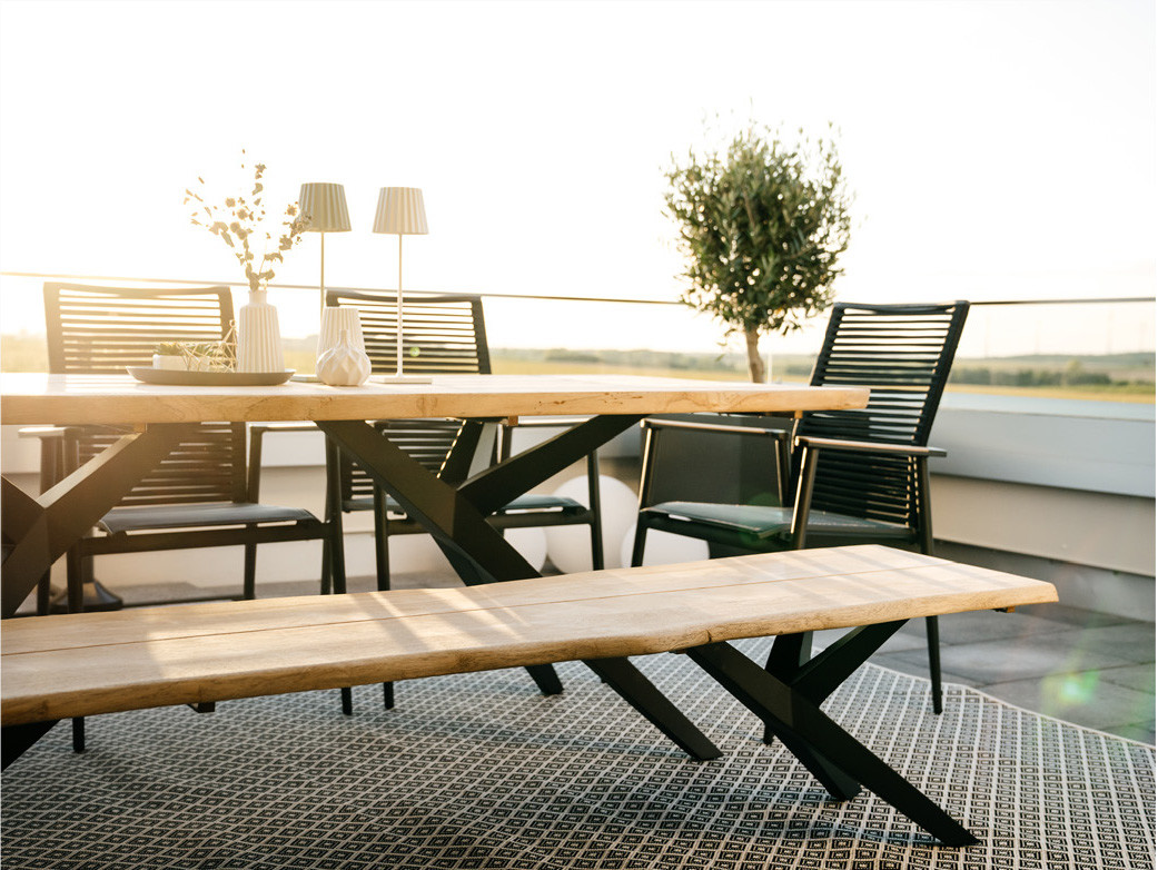 Terrasse mit Holztisch, Musterring Gartenmöbeln und Blick auf Gartenlandschaft.
