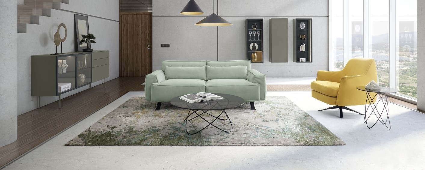 WK Polstermöbel WK Wohnen - Grünes Zweisitzer - WK Sofa und gelber WK Sessel mit Couch- und Beistelltisch. An der linken Raumwand ein WK Sideboard mit Vitrineneinsatz und im Hintergrund drei Hängeschränke.