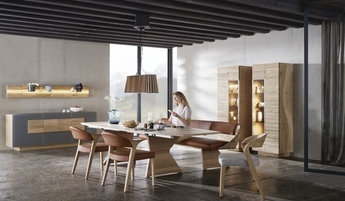 Voglauer Möbel Esszimmer helles Holz, grau, Esstisch, Stühle, Frau sitzt auf Bank, Vitrinen, Sideboard, Wandpaneel
