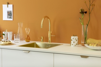 Goldener Quooker Fusion Wasserhahn mit oranger Wand im Hintergrund